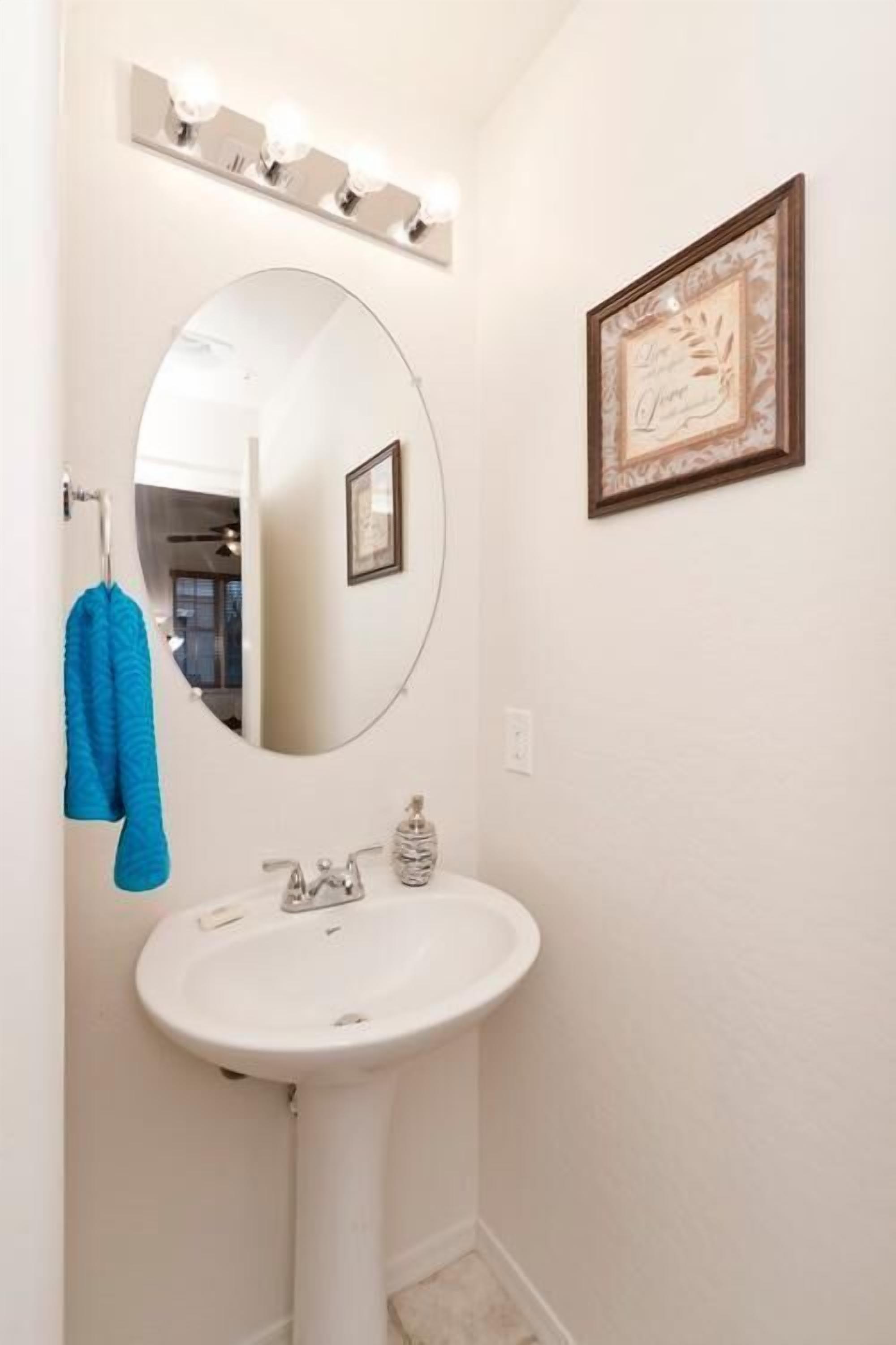 A bathroom with a white sink, a round mirror, and a framed picture on the wall.
