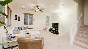 A spacious living room with a white sofa, a brown leather chair, a television, and a ceiling fan.