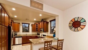 A kitchen with wooden cabinets, a granite countertop, and a clock on the wall.