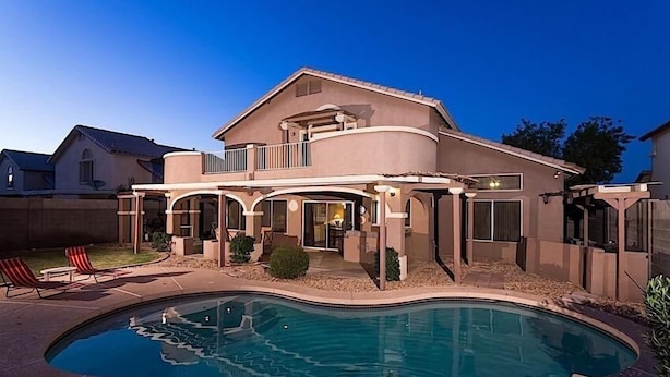 Una casa de dos pisos con piscina, un patio cubierto y un patio trasero cercado.