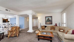 Ein geräumiges Wohnzimmer mit einer Eckcouch, einem Couchtisch und einem gemusterten Sessel.