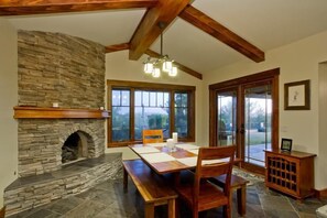 A dining area with a stone fireplace, wooden beams, large windows, and a view of the outdoors. - Majestic Carefree Home By Signature Vacation Rentals (Carefree)