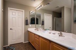 A bathroom with a double sink vanity, a large mirror, and a shower area. - Madelines Cottage By Signature Vacation Rentals (Surprise)