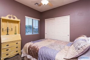 Un dormitorio con cama, cómoda, ventana con persianas, puerta y ventilador de techo.