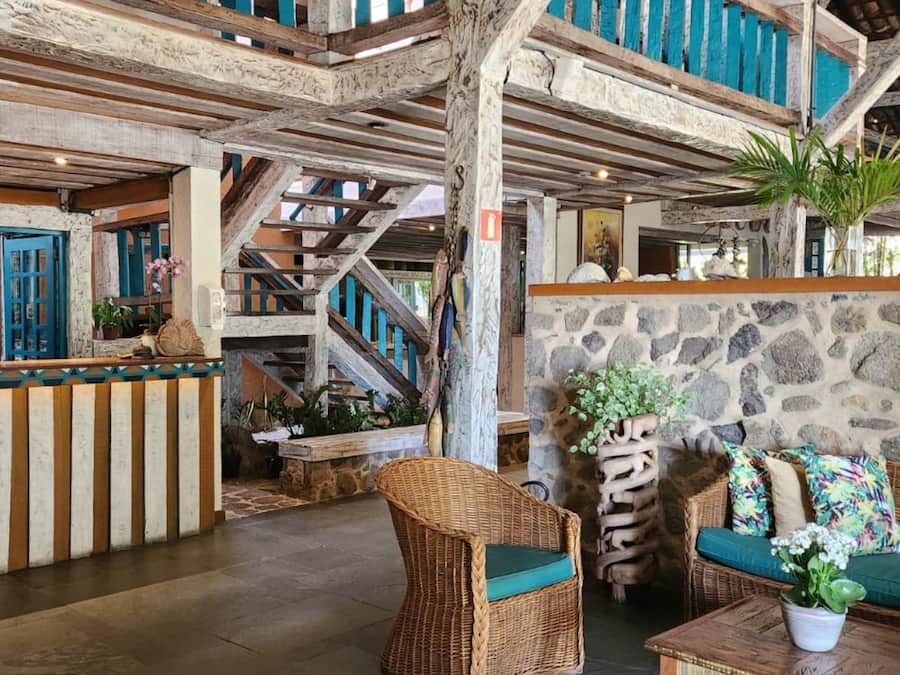 A lobby with a reception desk, wicker furniture, a staircase, and stone walls.