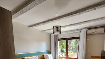 Habitación de hotel con dos camas, techo de madera, ventilador de techo, ventana con cortinas y una pequeña mesa con lámpara.