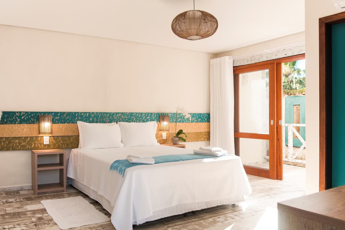 Hotelkamer met een bed, nachtkastjes, een lamp, uitzicht door een glazen deur en een houten bank.