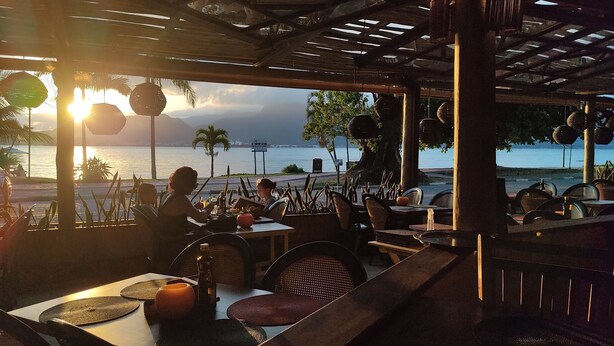 An outdoor restaurant with tables and chairs, overlooking a body of water and mountains.