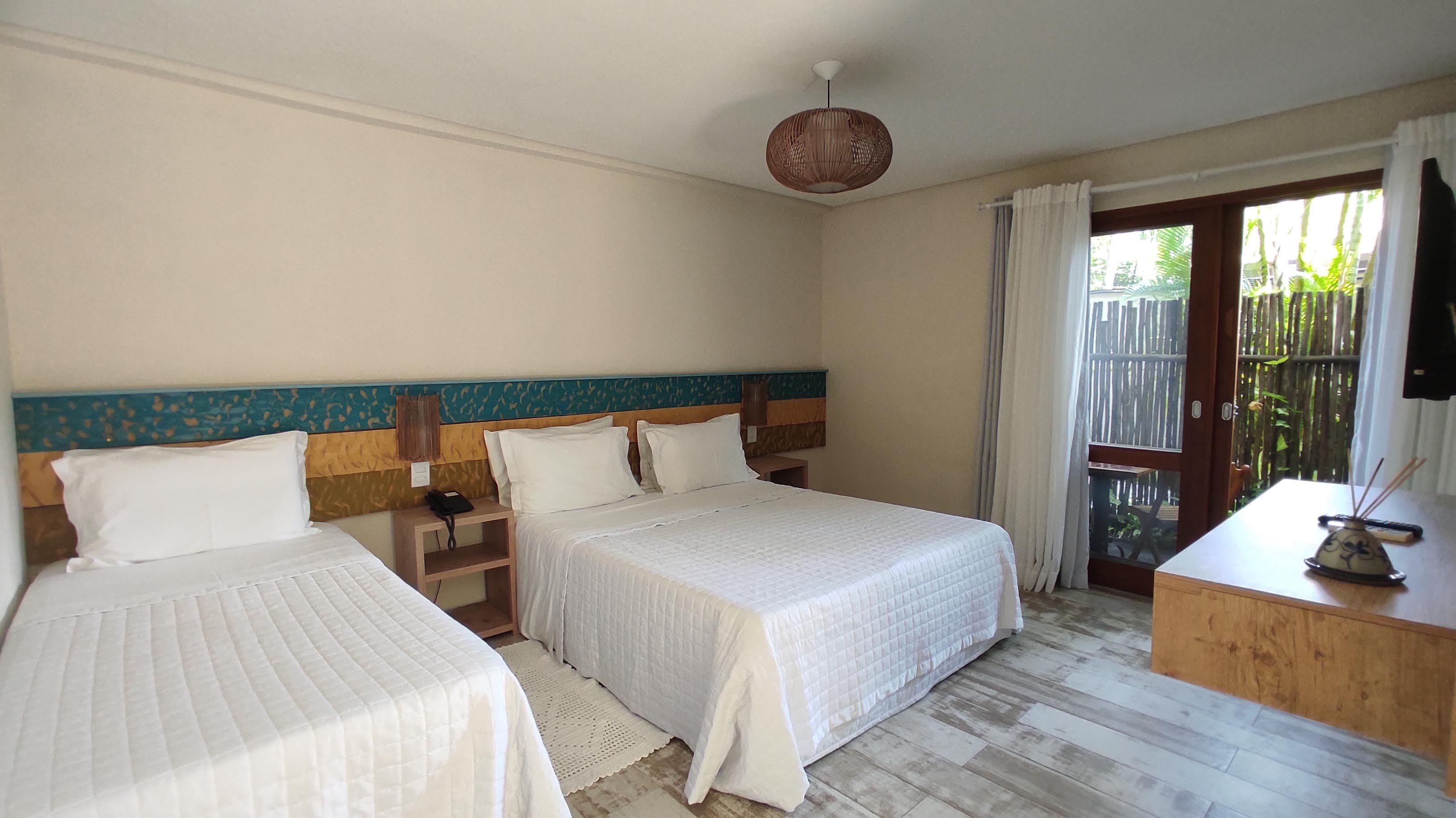 A hotel room with two beds, a wooden headboard, a nightstand, a desk, and a view of the outdoors.