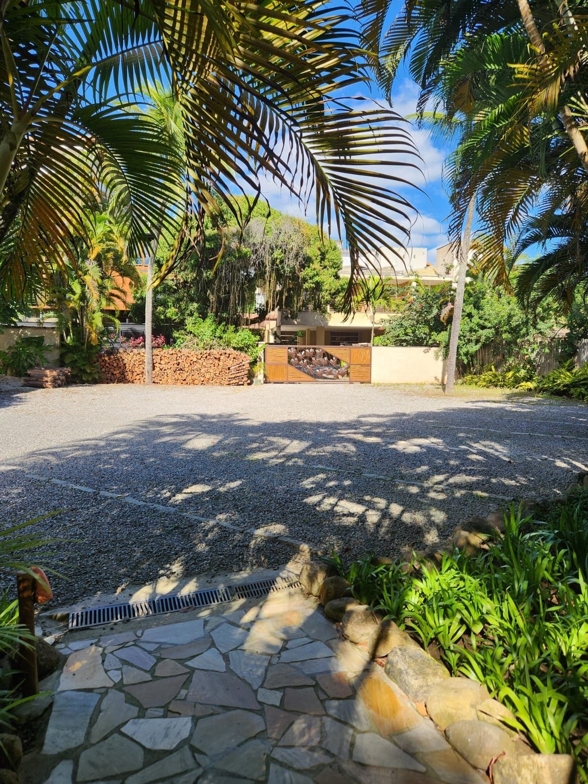 A paved driveway leading to a gated entrance with a stone pathway and lush greenery.