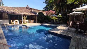 A swimming pool with a wooden deck, surrounded by lounge chairs and umbrellas.