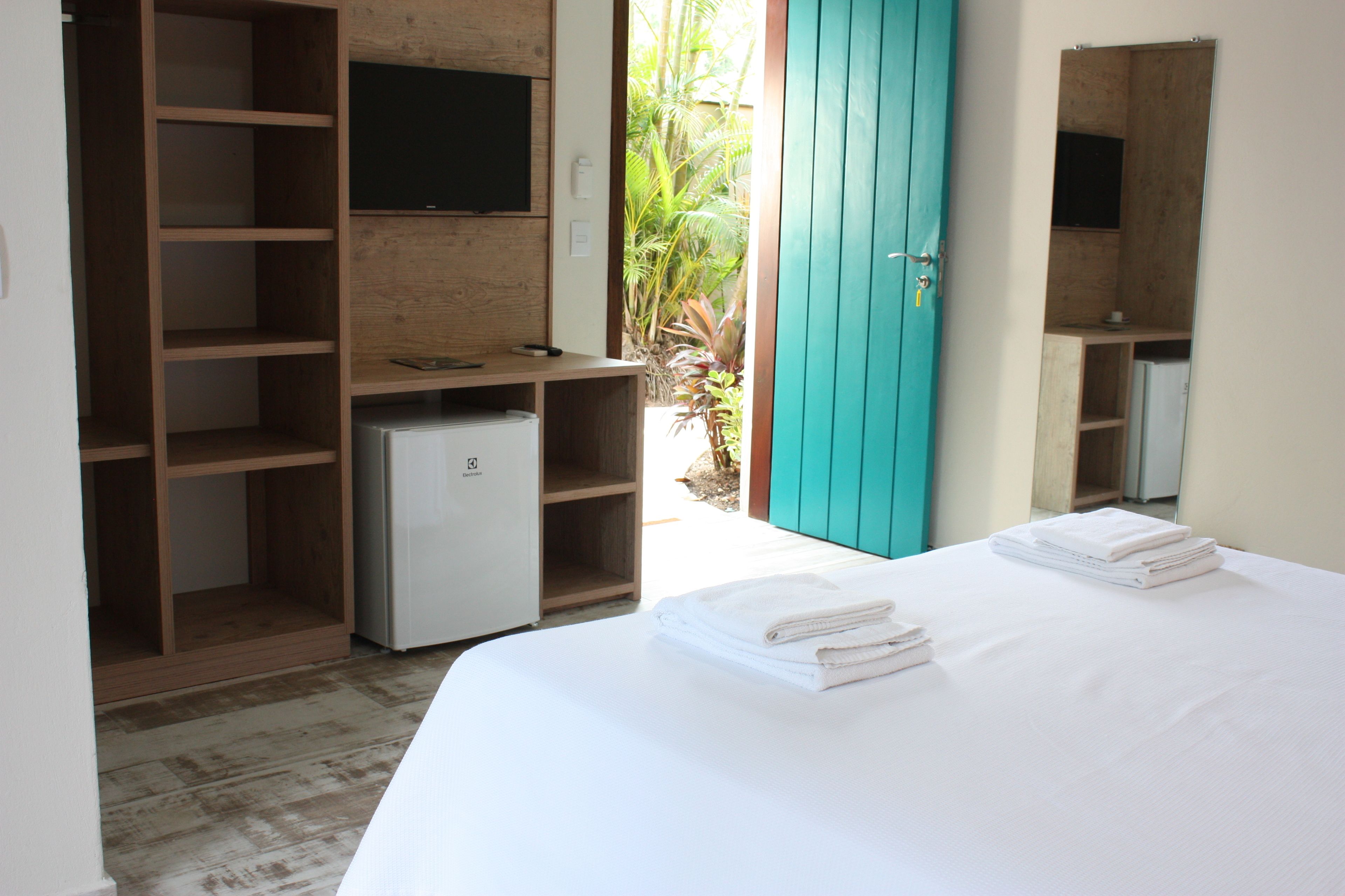 Un dormitorio con una cama, un televisor montado en un estante de madera, un refrigerador pequeño y una puerta verde azulada.