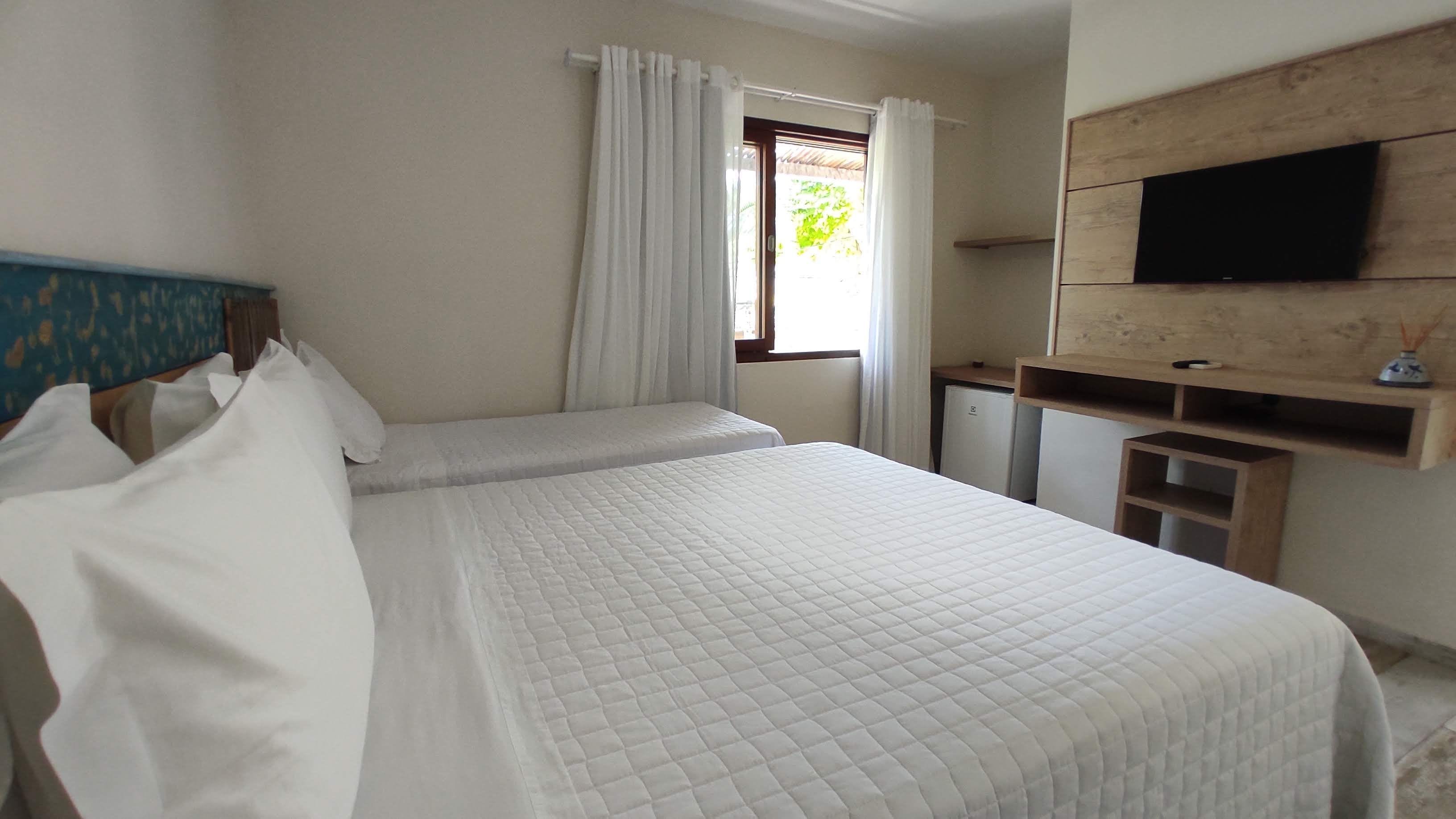 Une chambre d’hôtel avec un lit, un téléviseur fixé au mur et une fenêtre avec des rideaux.
