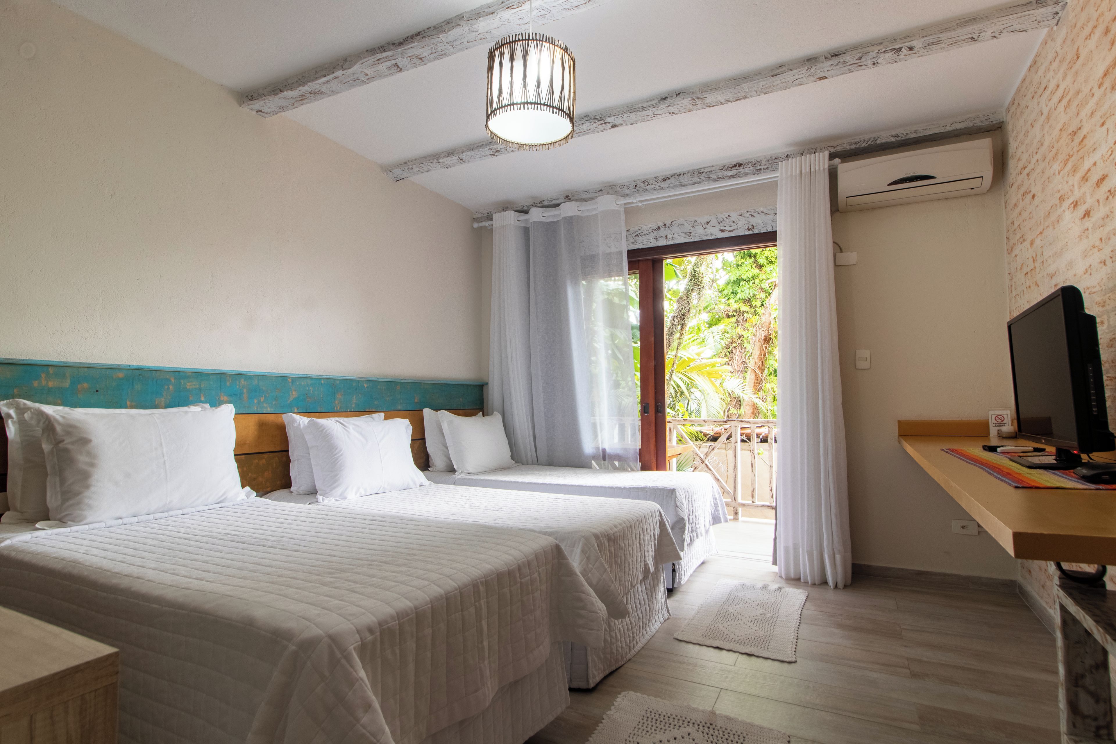 A hotel room with two beds, a desk with a computer, and a view of the outdoors.