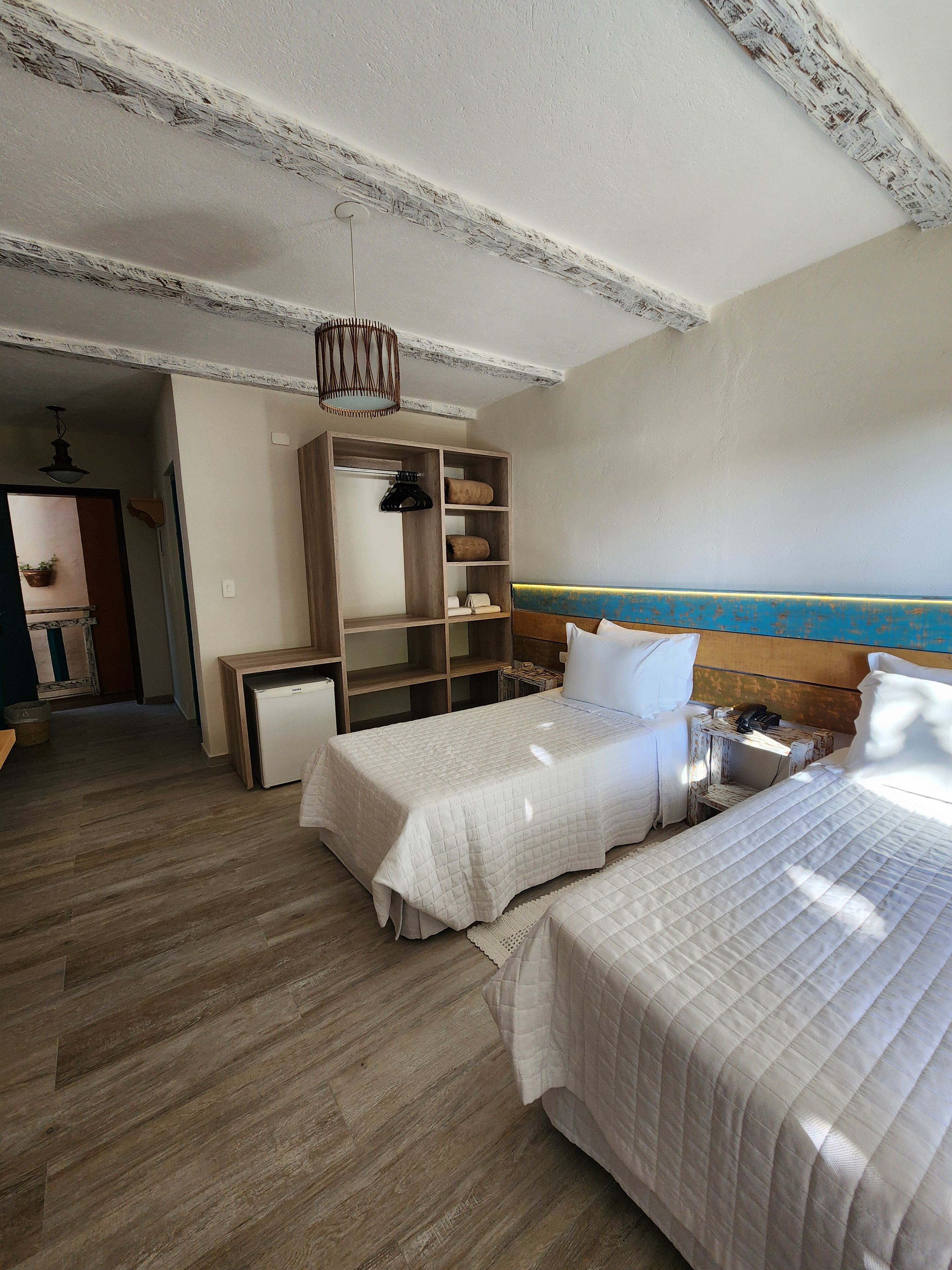 A hotel room with two beds, a wooden wardrobe, a small desk, and a view of the sea.