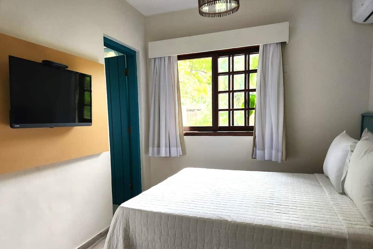 Een slaapkamer met een bed, een aan de muur bevestigde televisie, een raam met gordijnen en een deur.