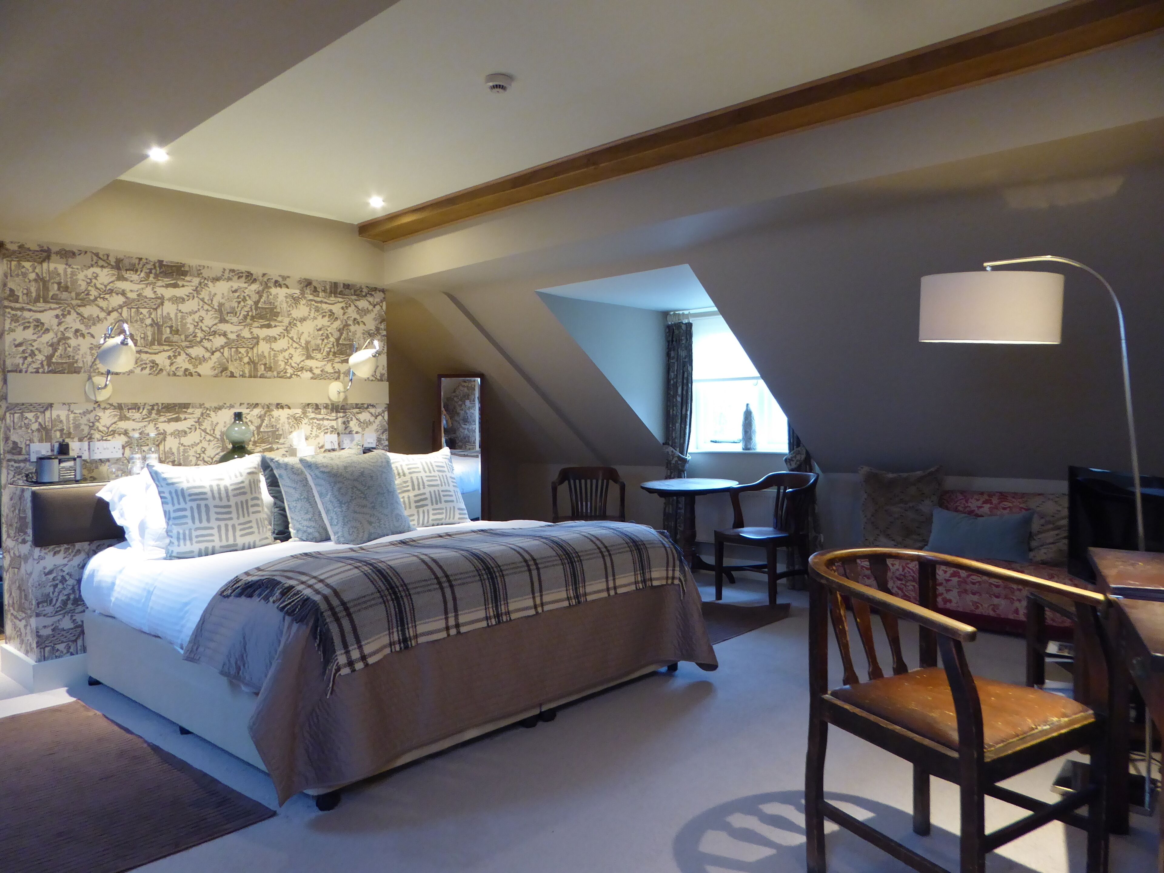 A bedroom with a bed, bedside tables, a desk, and a chair. There is a window with curtains and a lamp.