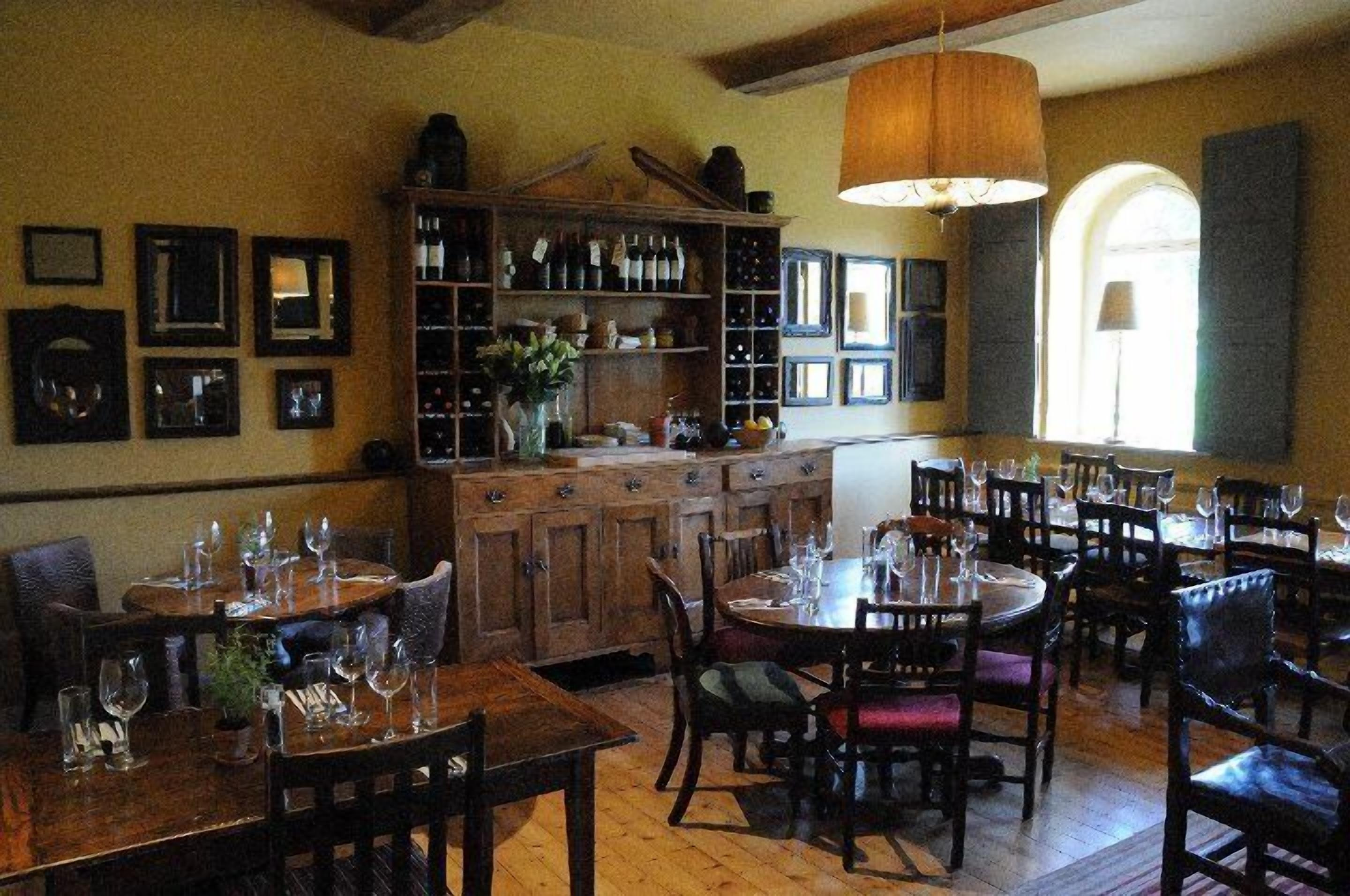Un restaurante con mesas y sillas de madera, una estantería para vinos y cuadros en las paredes.