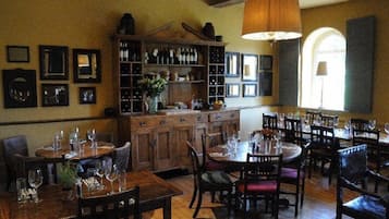 Un restaurante con mesas y sillas de madera, una estantería para vinos y cuadros en las paredes.