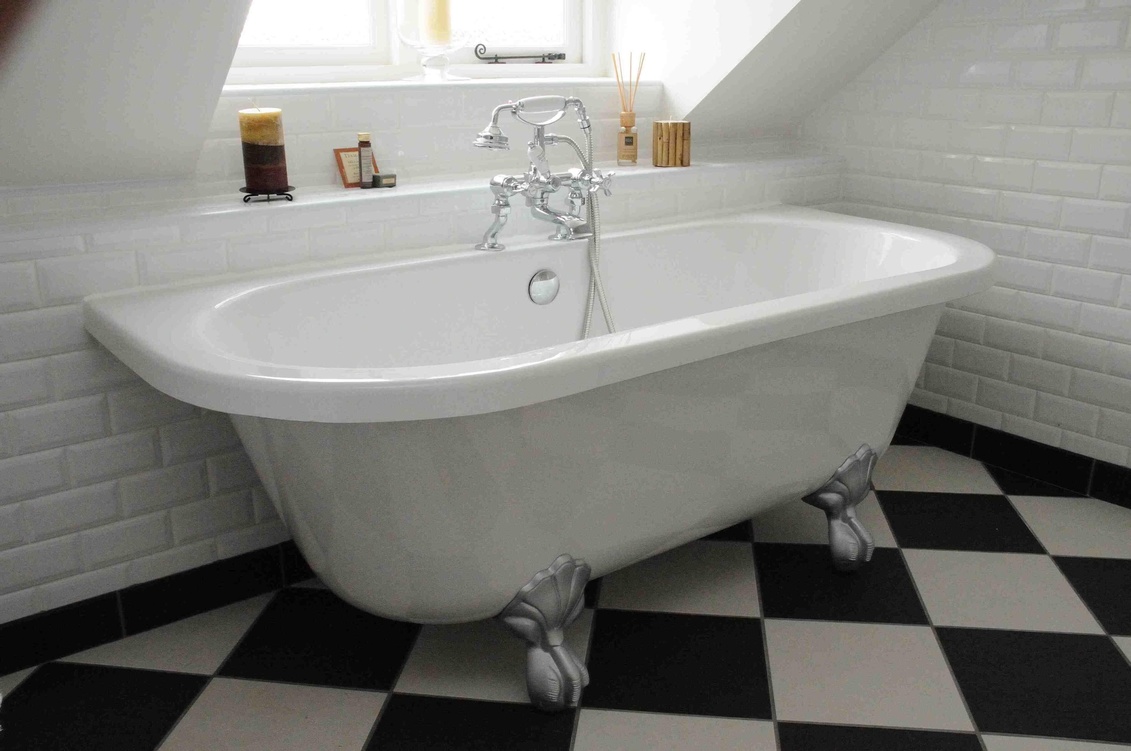 A bathroom with a freestanding bathtub, white tiled walls, and a black and white checkered floor.