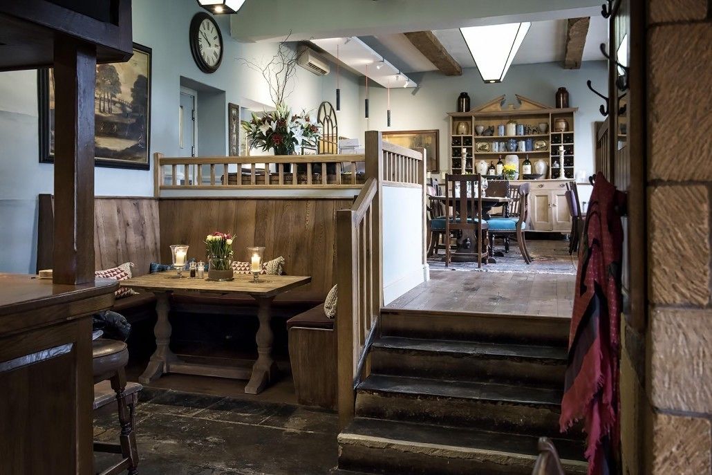 A cozy interior with a wooden staircase, a dining area with a table and benches, and a bookshelf filled with books and decorative items.