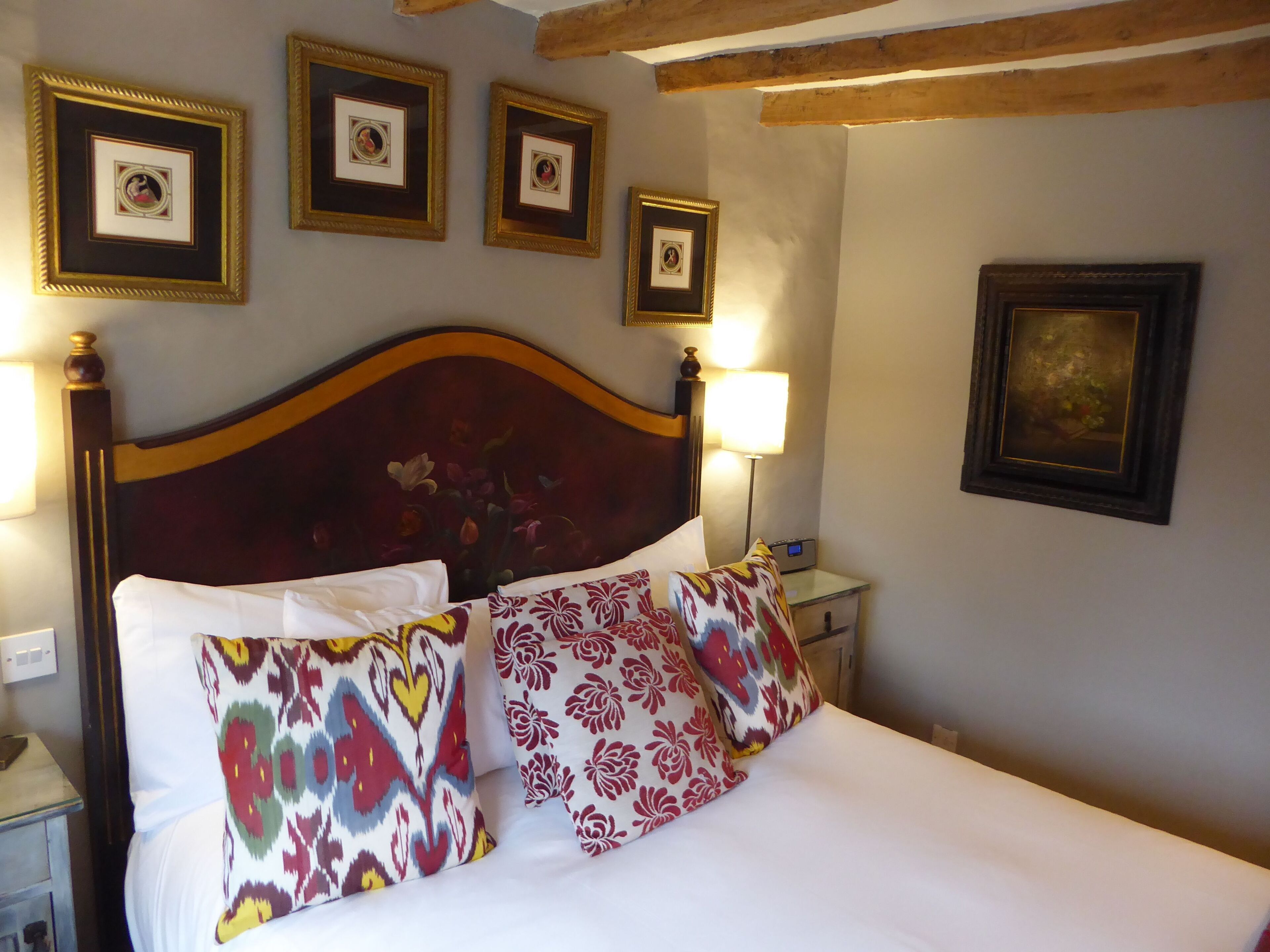 A neatly made bed with patterned pillows, a wooden headboard, and framed pictures on the wall.