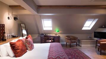A bedroom with a bed, a desk, a chair, a TV, and skylights.