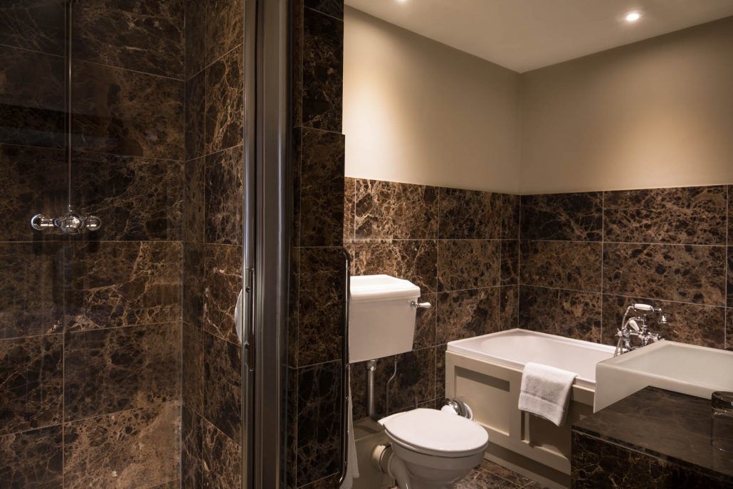 Un baño con ducha, inodoro y bañera, todo con paredes y accesorios de mármol.