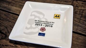 A square white plate with text and logos, placed on a wooden surface.
