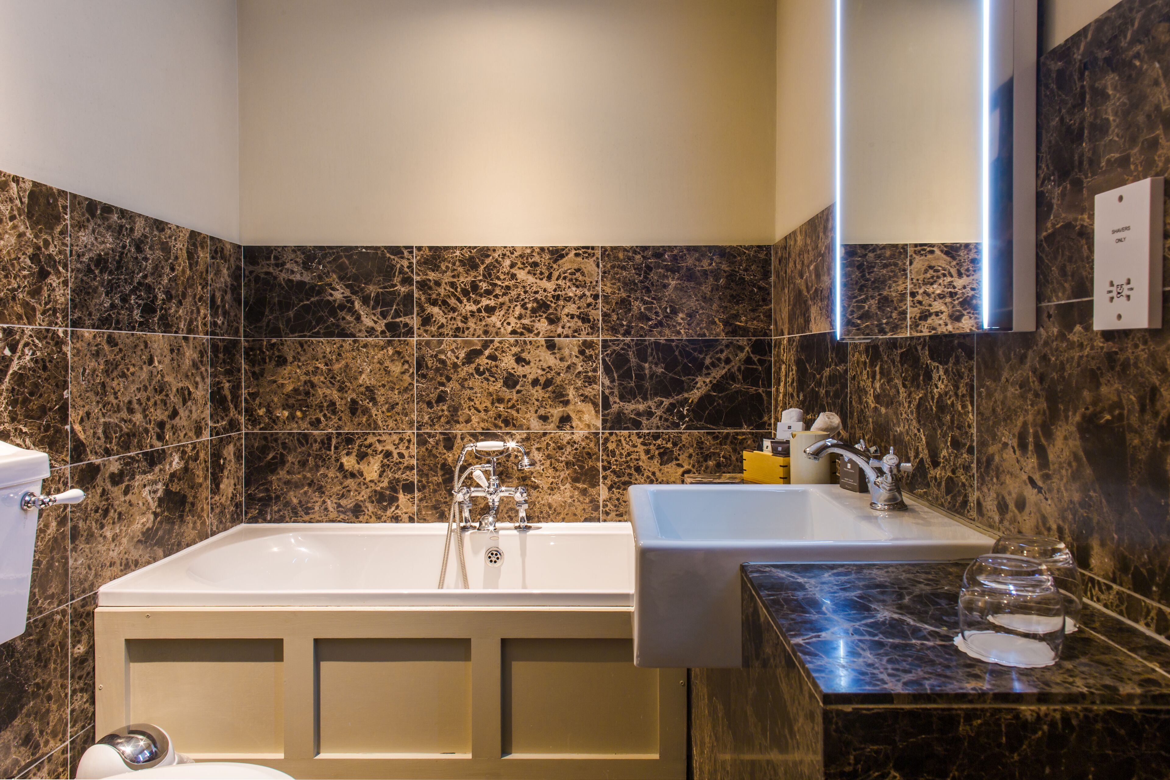 A bathroom with a bathtub, a sink, and a marble-tiled wall.