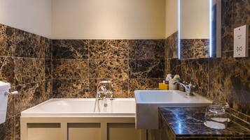 A bathroom with a bathtub, a sink, and a marble-tiled wall.