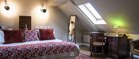A bedroom with a large bed, a desk, and a chair. There is a skylight above the bed and a mirror on the wall.