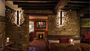 A rustic interior with stone walls, a fireplace, and wooden furniture. - The Howard Arms (Shipston on Stour)