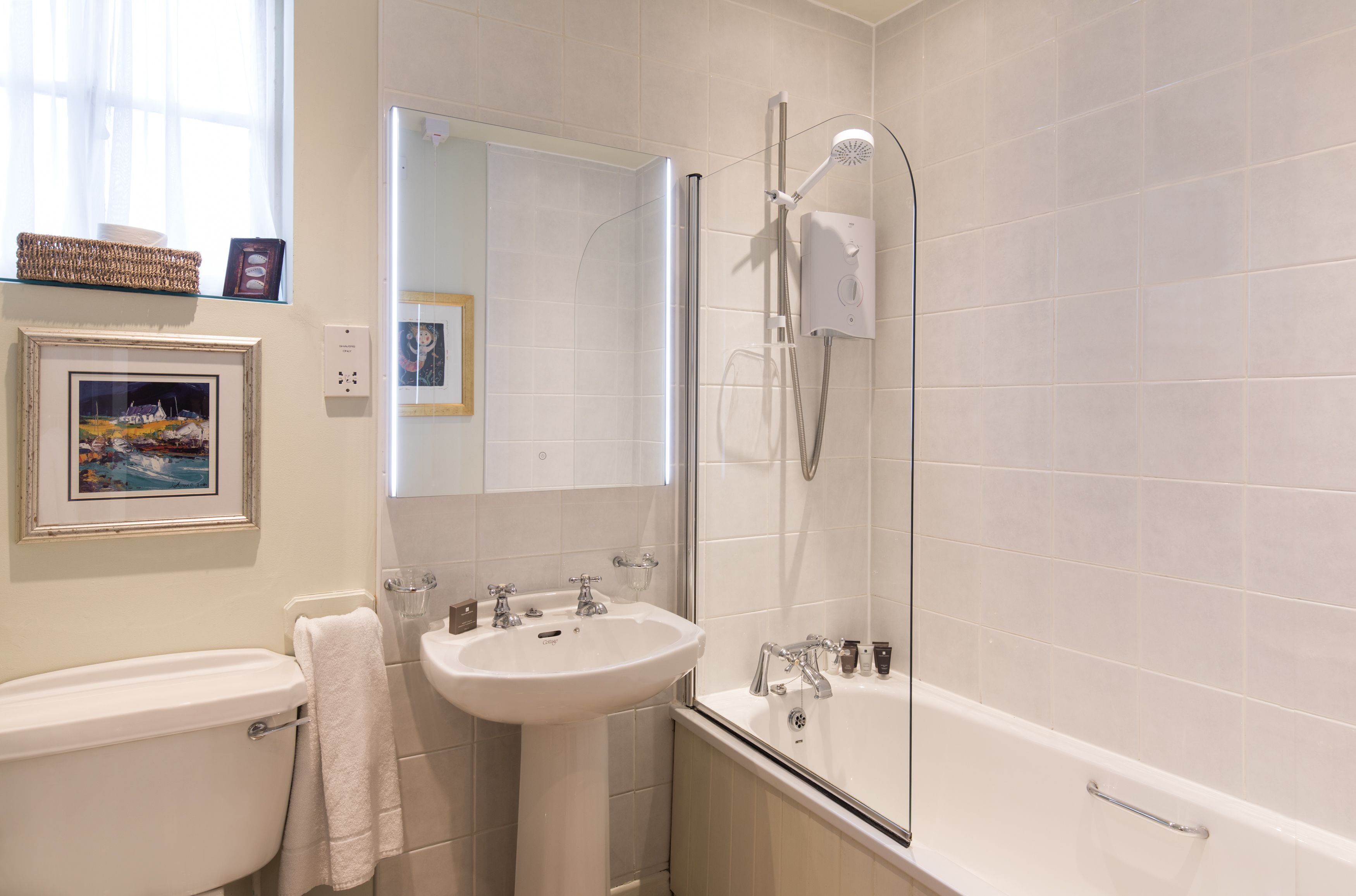 Une salle de bain moderne équipée de toilettes, d’un lavabo et d’une baignoire. On y trouve également une douche avec une porte en verre et un miroir au-dessus du lavabo.