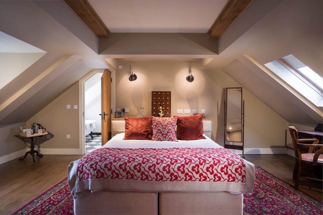 A bedroom with a large bed, two pendant lights, a skylight, and a view of a hallway.
