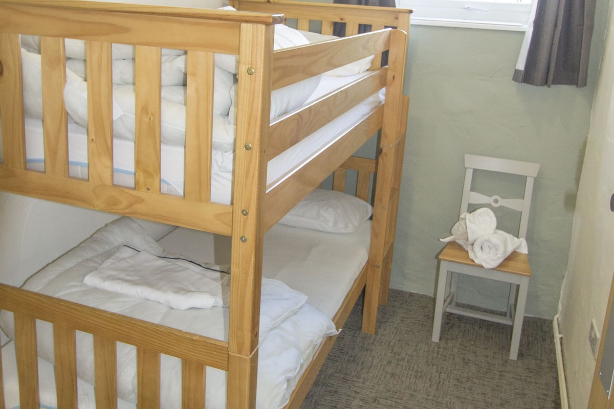 A bunk bed room with a small chair and a window with curtains.