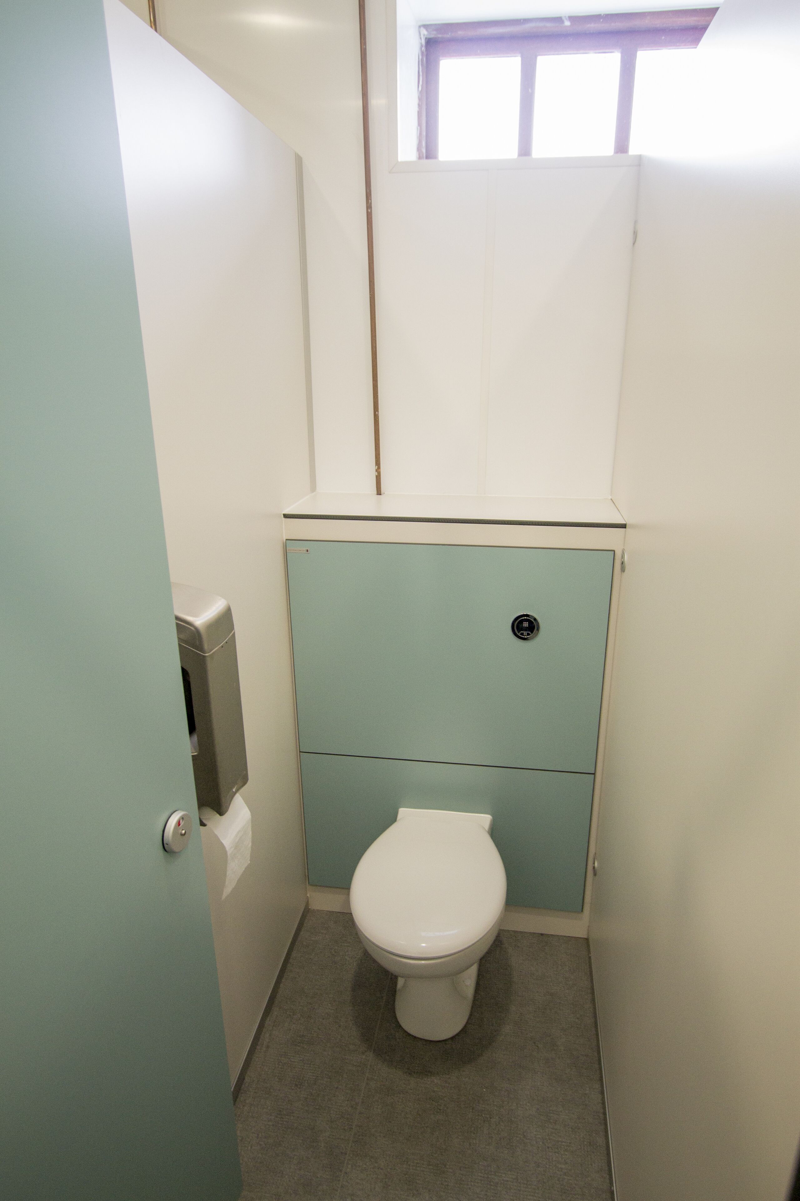 Um banheiro pequeno e compacto, com vaso sanitário, dispensador de toalhas de papel e uma janela sobre o vaso.
