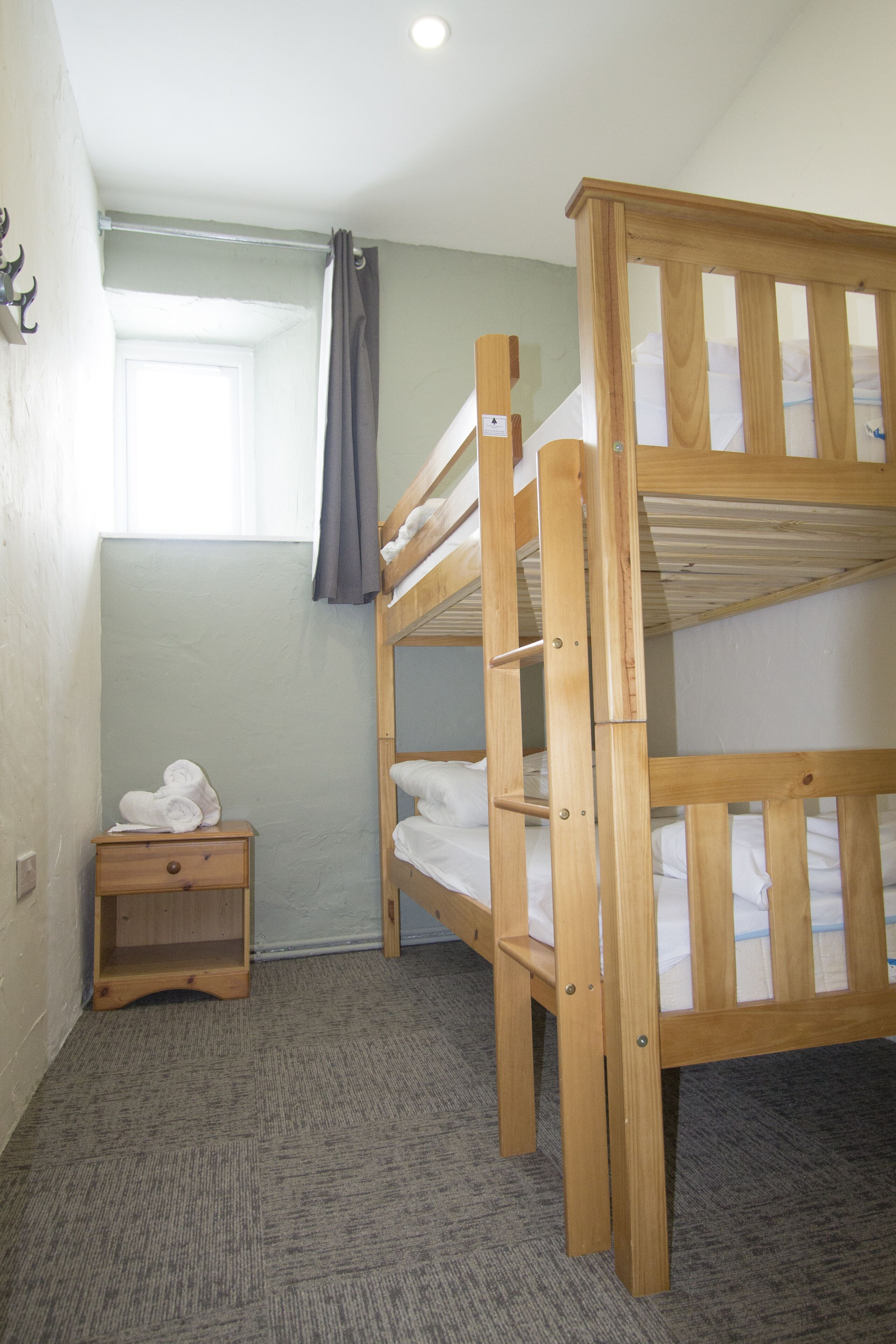 Habitación con literas, una mesita de noche de madera y una ventana con cortinas.
