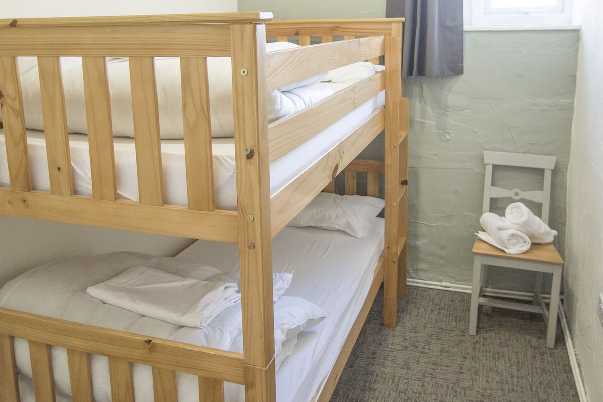A bunk bed with two levels, a small wooden chair, and a window with curtains.