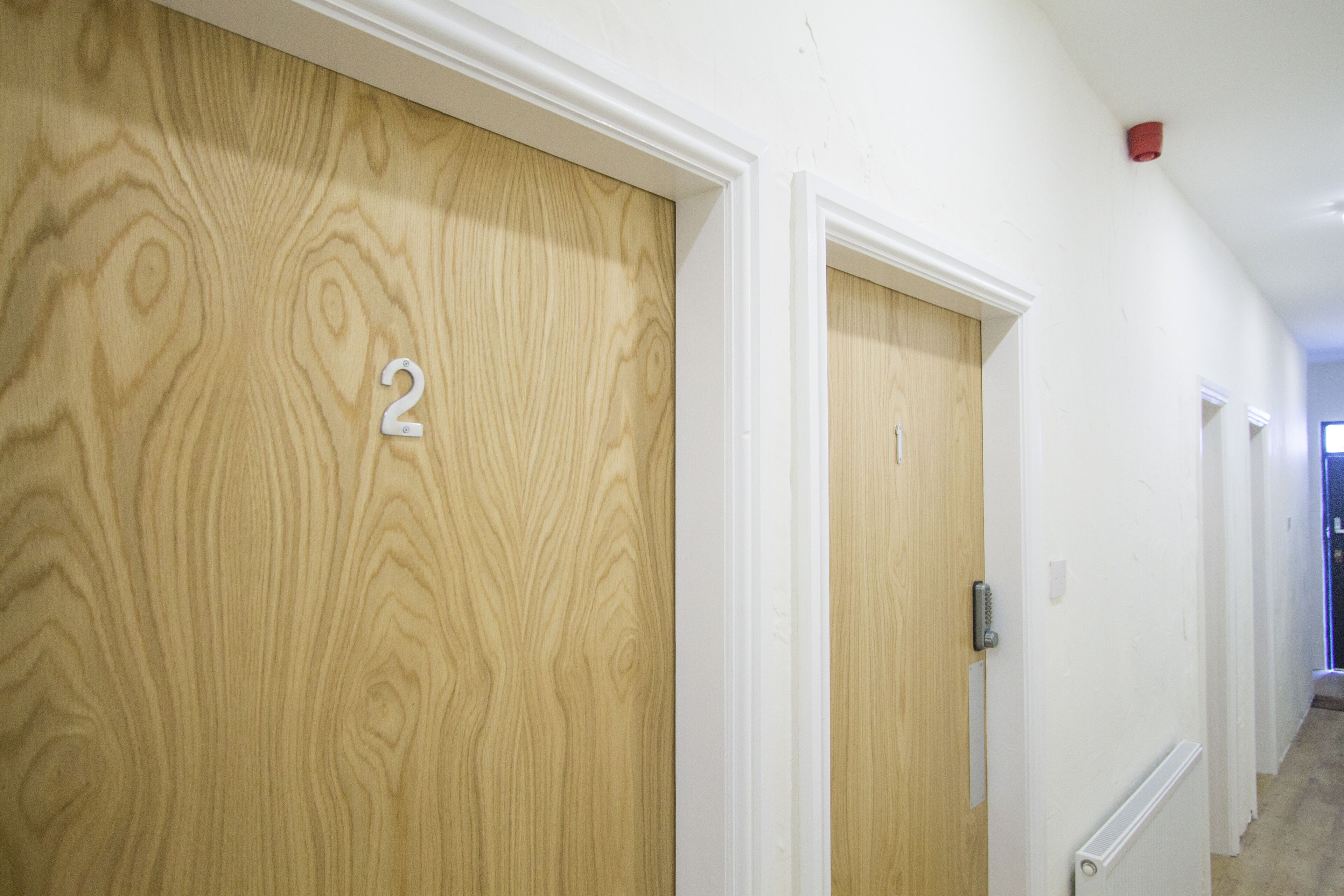 A hallway with wooden doors numbered 1 and 2, white walls, and a red ceiling light.