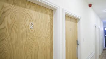 A hallway with wooden doors numbered 1 and 2, white walls, and a red ceiling light.