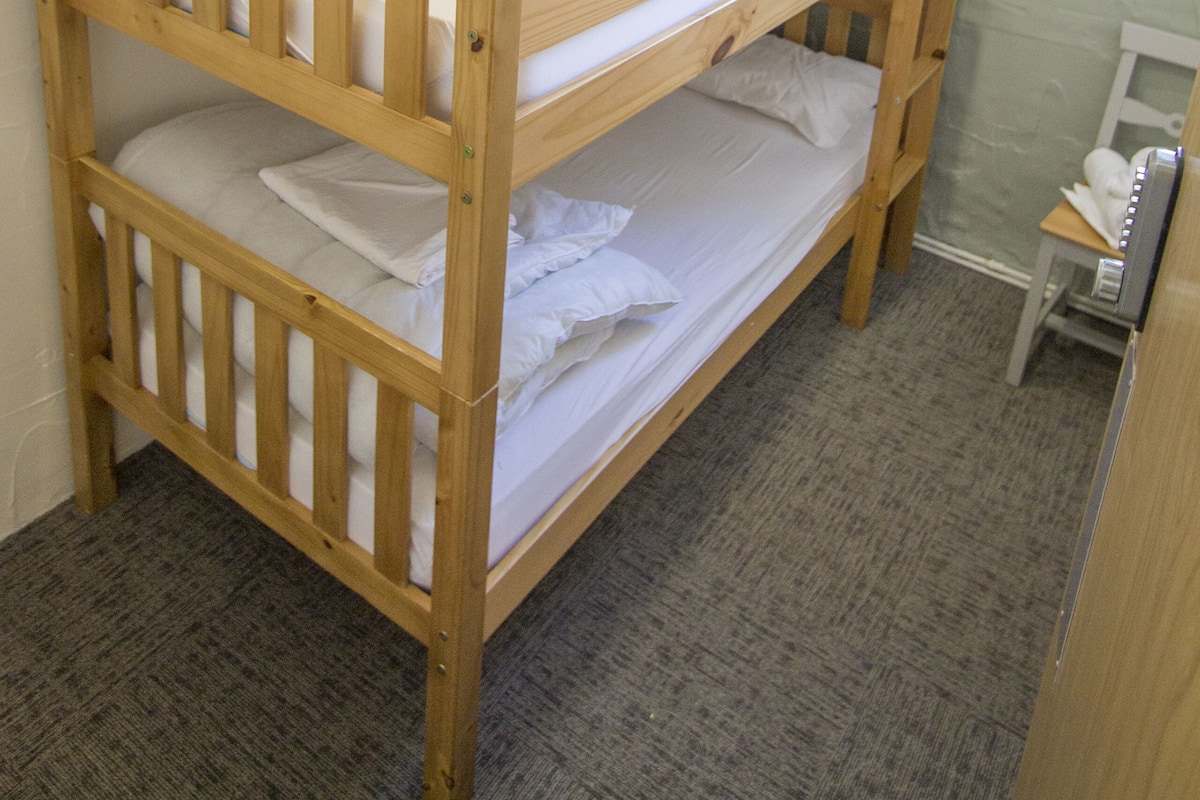 A bunk bed in a room with a carpeted floor and a window with curtains.