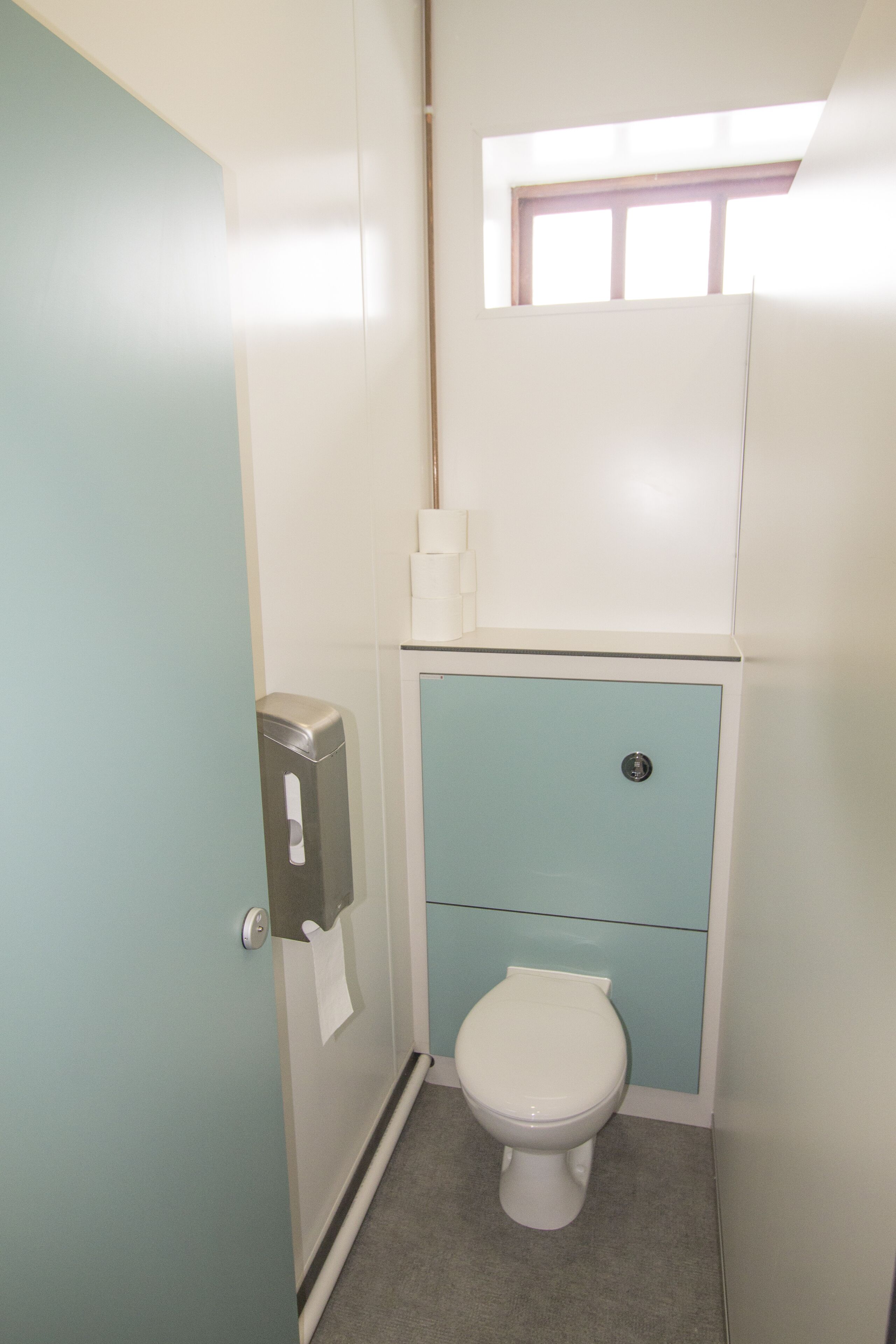 A small, compact bathroom with a toilet, a hand dryer, and a window above the toilet.