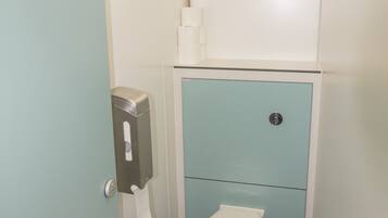 A small, compact bathroom with a toilet, a hand dryer, and a window above the toilet.
