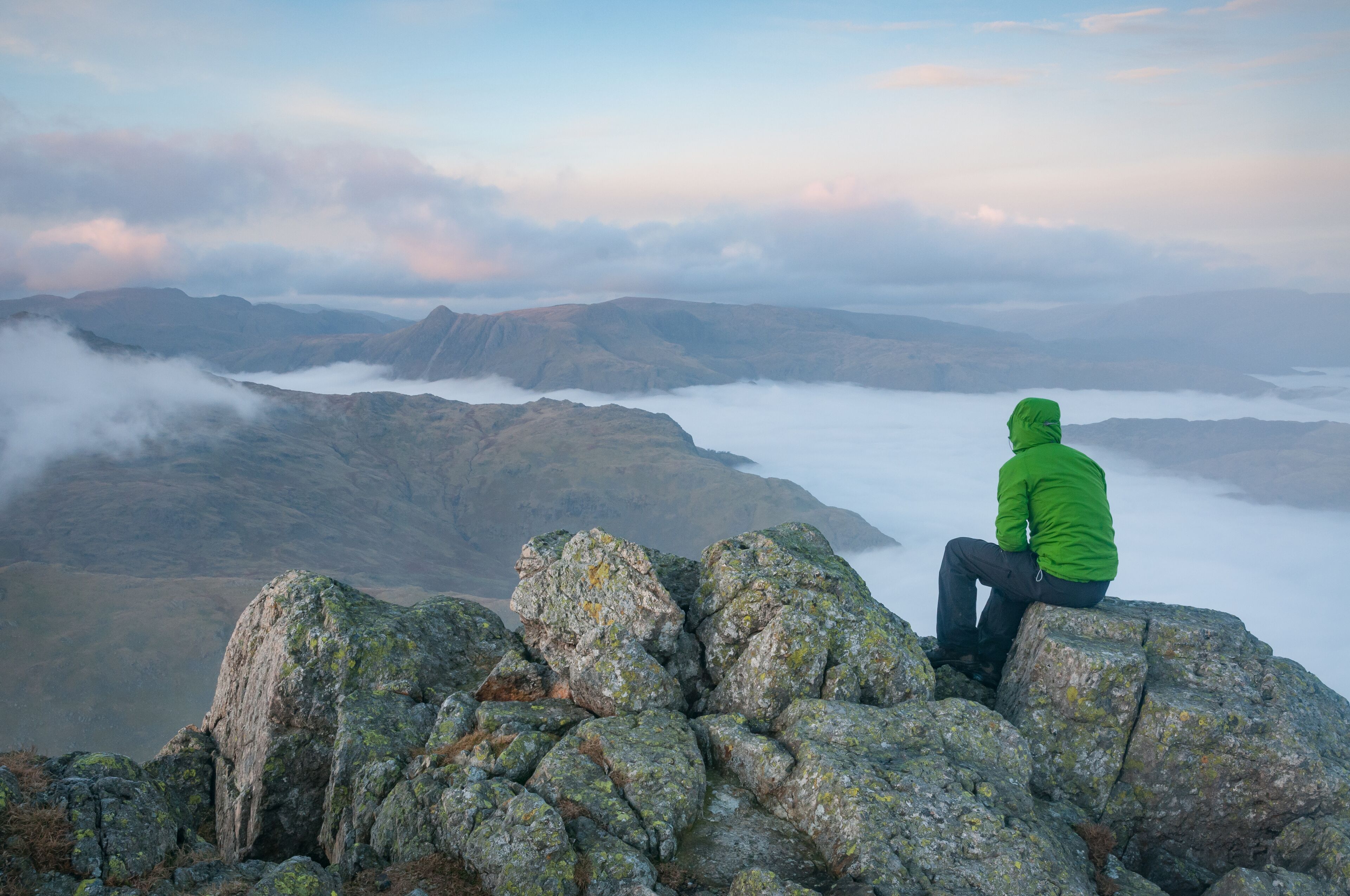 A person sitting on rocks overlooking a mountainous landscape with fog.