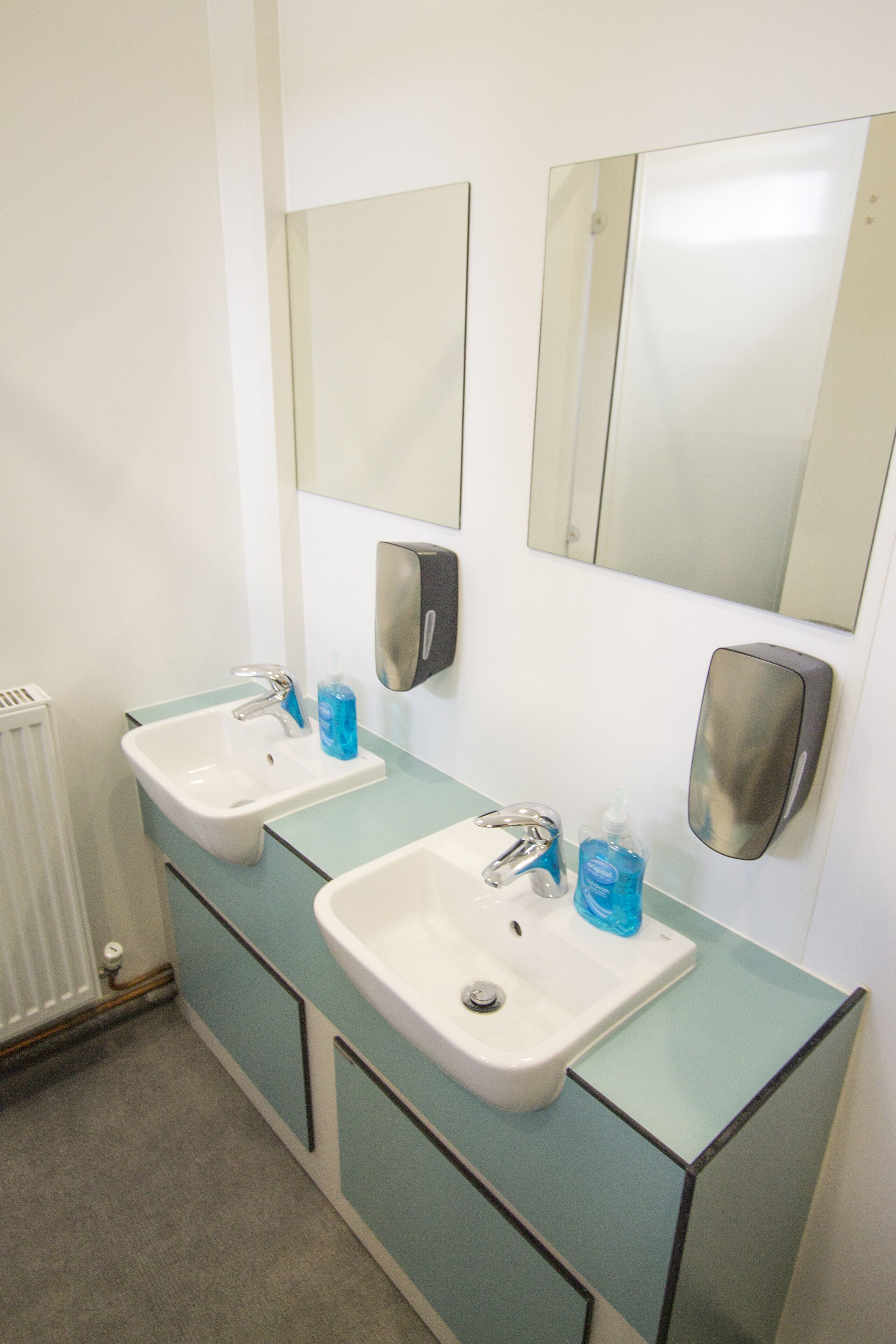 A bathroom with two sinks, a mirror, and a hand sanitizer dispenser.