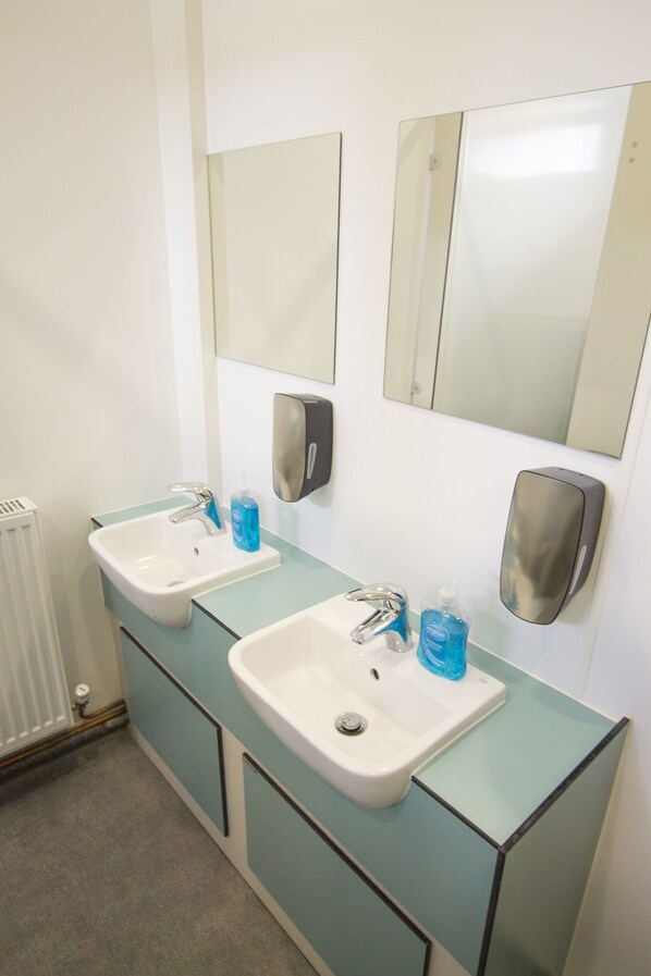 A bathroom with two sinks, a mirror, and a hand sanitizer dispenser. - Great Langdale Bunkhouse Hostel (Ambleside)
