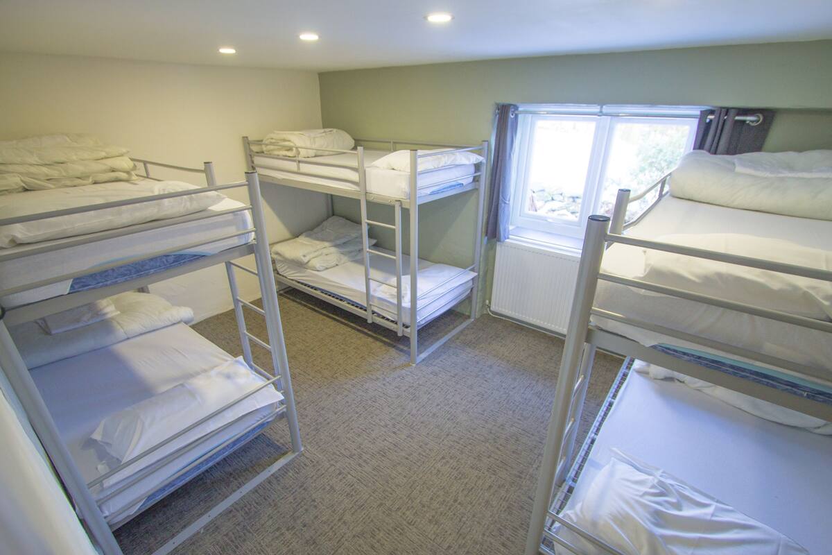A bunk bed room with three bunk beds, a window with curtains, and a radiator.