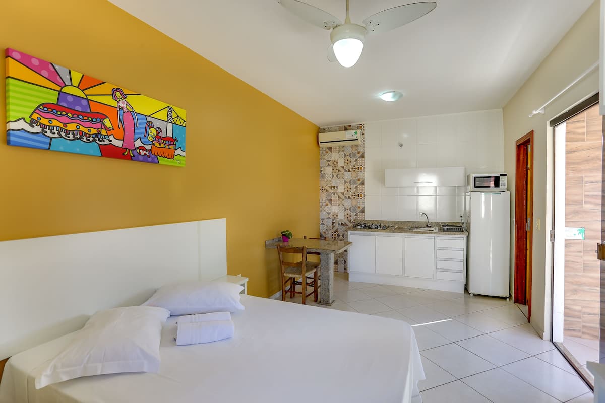 A hotel room with a bed, a small table with chairs, a kitchenette, and a colorful mural on the wall.