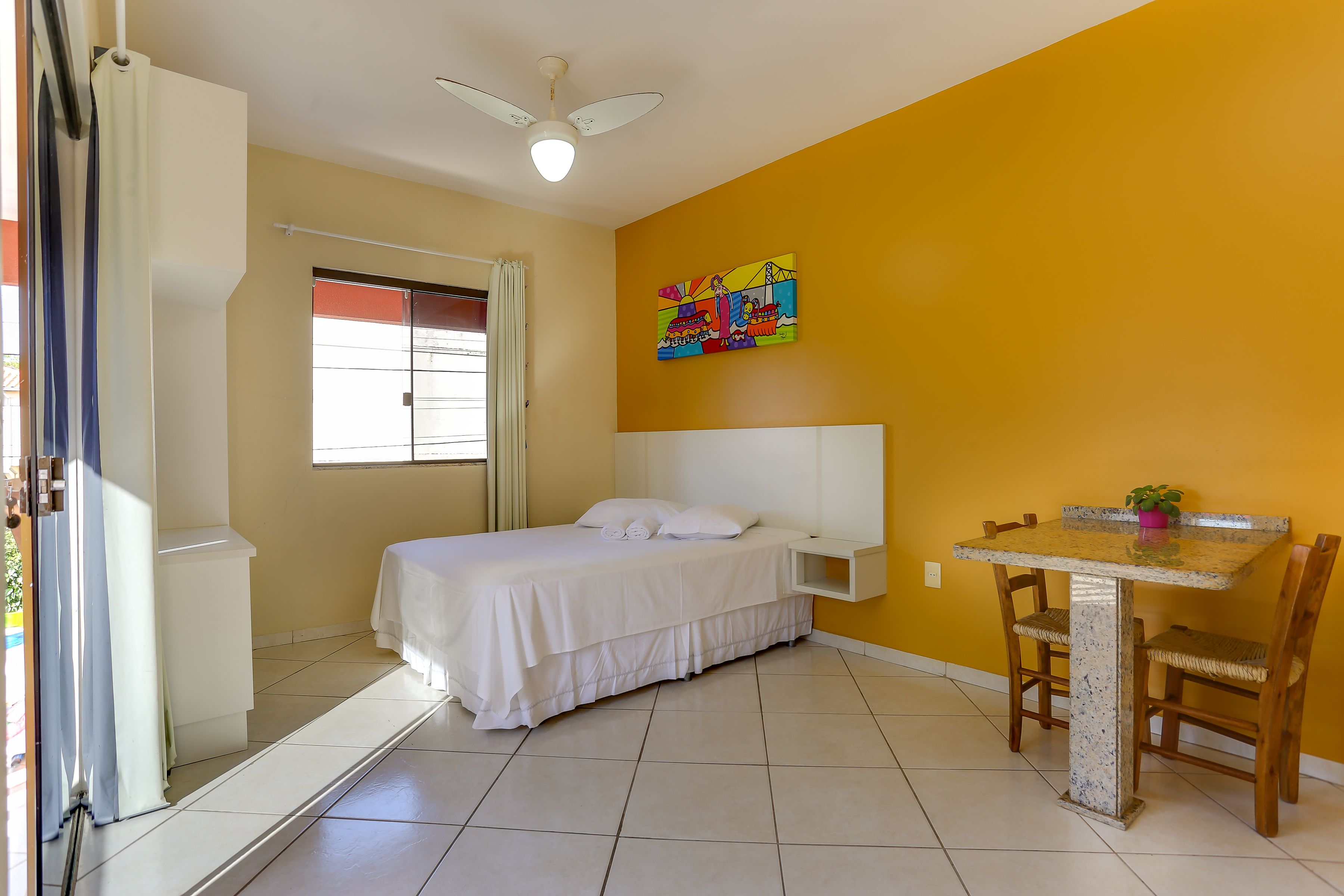 A room with a bed, a small table, and a ceiling fan.